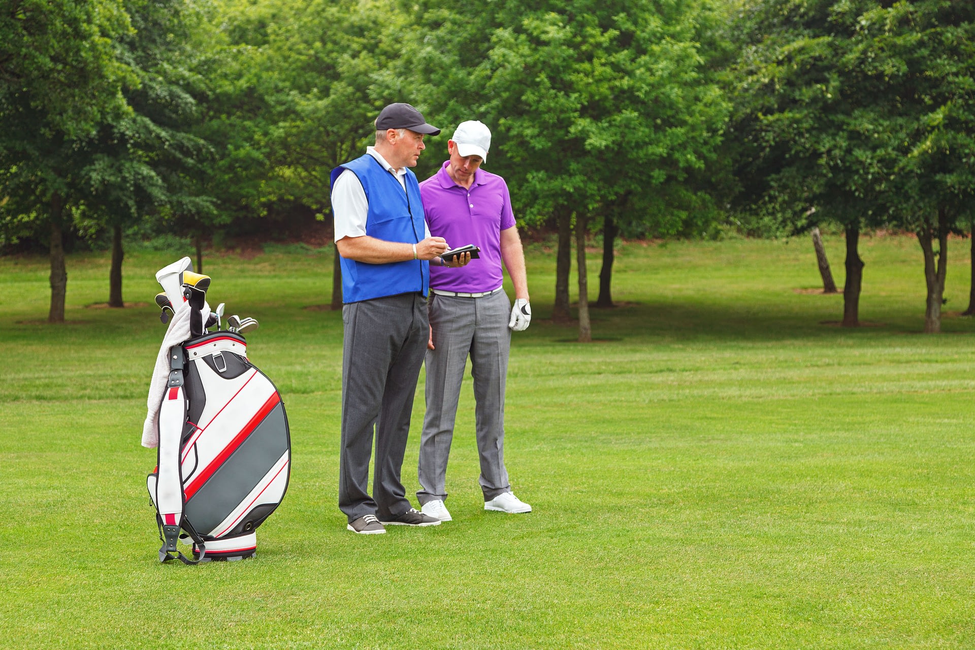 Golfer and caddy standing on the fairway of a par 4 looking at a course guide.